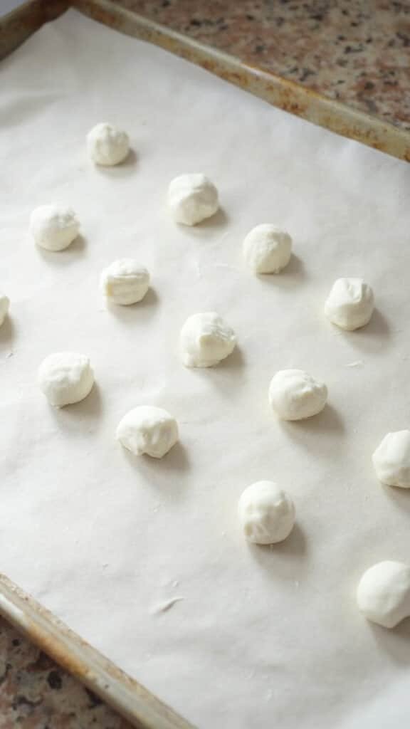 Small uniform balls of marble countertop treat shaped on a parchment lined baking sheet under soft diffused light.