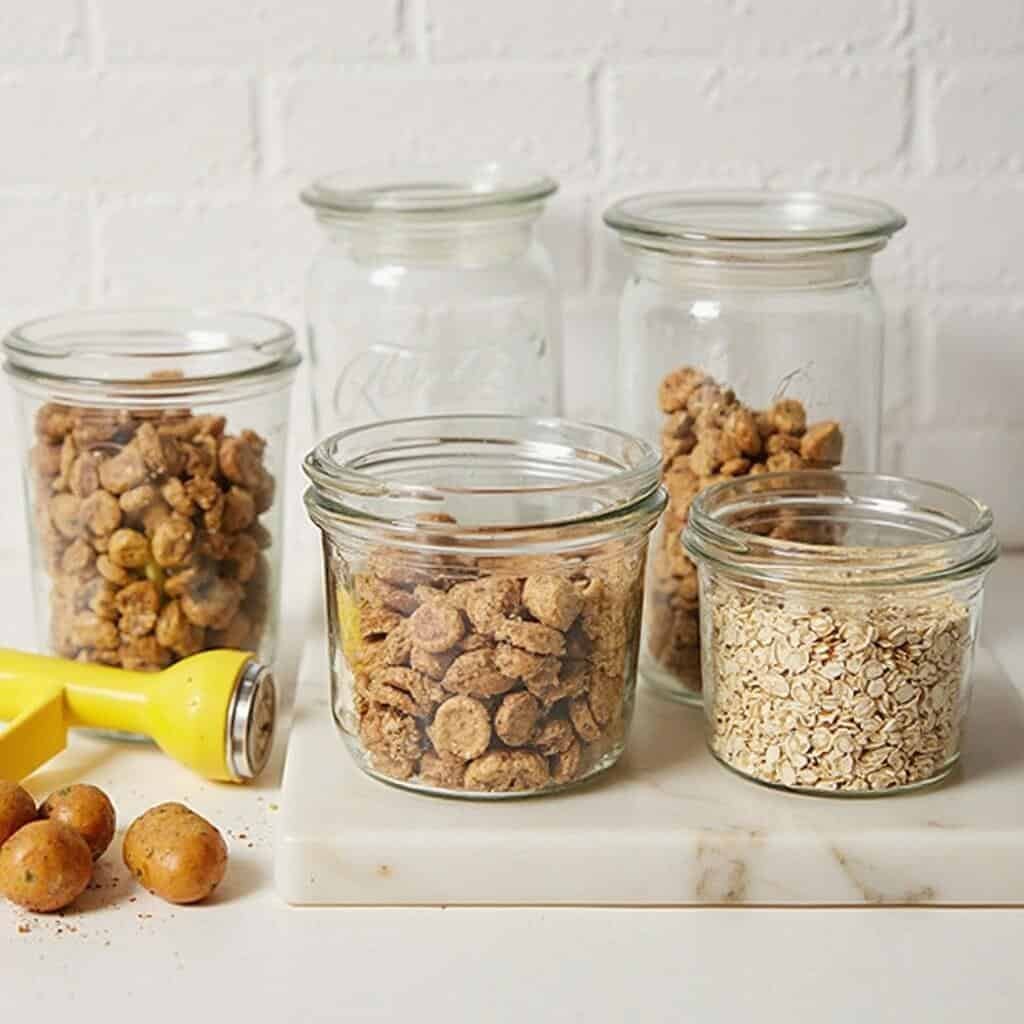 Portioned turkey oatmeal dog food in glass jars on a kitchen counter with a potato masher beside them