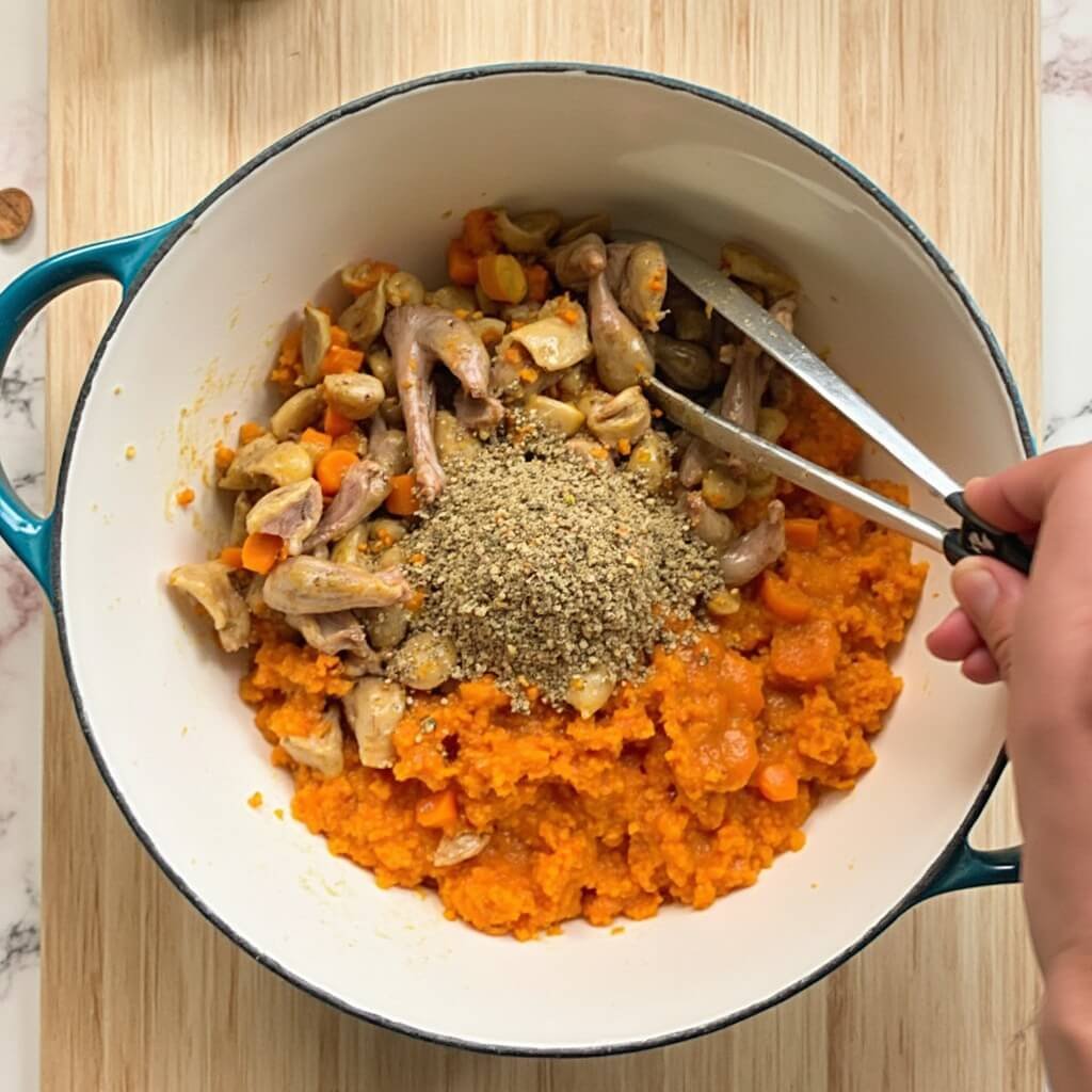 Mixing bowl of cooked duck offal and mashed carrot with supplement powder being stirred together