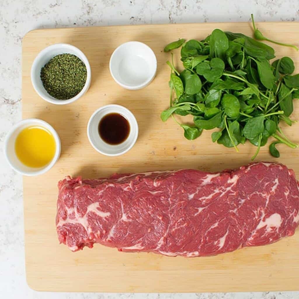 Raw rabbit meat and fresh spinach ingredients on a cutting board